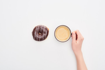 partial view of woman holding cup with coffee near tasty glazed chocolate doughnut on white...