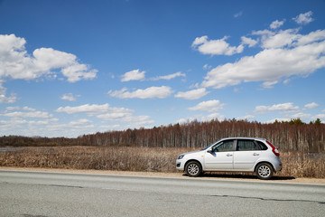 Fototapeta na wymiar Car on asphalt road in early spring near forest and blue sky with clouds. Landscape in in nice spring day. Russia