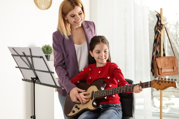 Little girl playing guitar with her teacher at music lesson. Learning notes