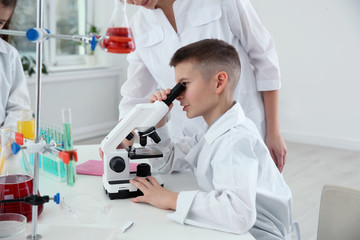Naklejka na ściany i meble Schoolboy looking through microscope at table in chemistry class