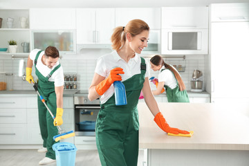 Woman using rag and sprayer for cleaning table with colleagues in kitchen