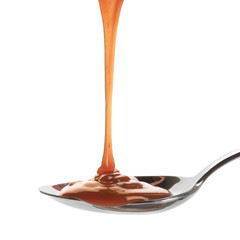 Tasty caramel sauce pouring into spoon isolated on white