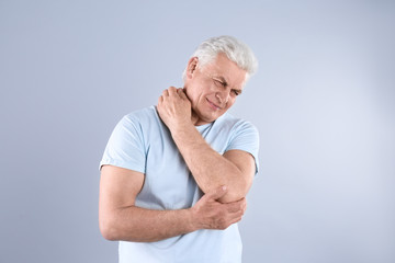 Senior man scratching neck on grey background. Allergy symptom