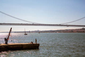 Man fishing on river with suspension bridge on the background