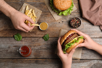 People with burger and French fries at wooden table, top view