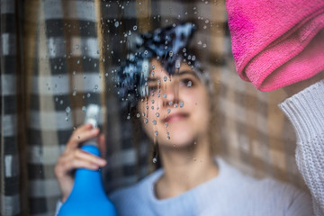 Cute girl with smile on her face cleaning the window with pink rag.