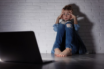 Scared teenage girl with laptop on floor in dark room. Danger of internet