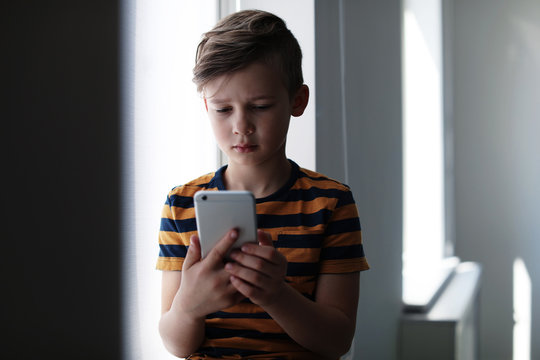 Sad little child with smartphone indoors. Danger of internet