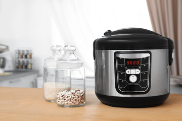 Jars with rice and beans near modern multi cooker on table in kitchen