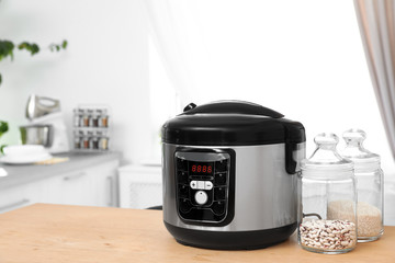 Jars with rice and beans near modern multi cooker on table in kitchen. Space for text