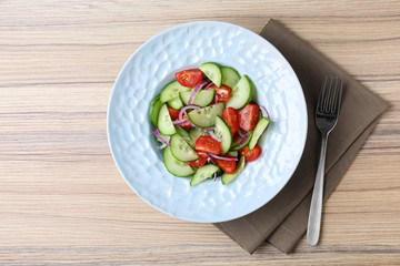 Plate of tasty cucumber tomato salad served on wooden table, flat lay