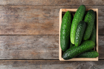 Crate full of fresh ripe cucumbers on wooden background, top view. Space for text