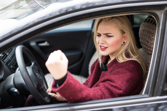 Picture of angry blond girl in white car showing fist on roadside. Young woman looking nervous after car incident.