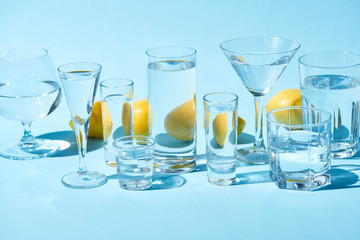 transparent glasses with water and whole lemons on blue background