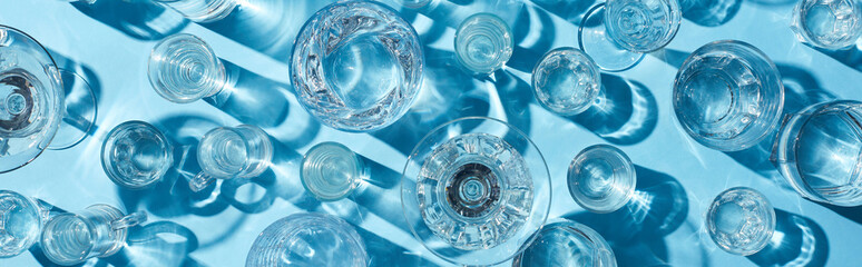 top view of glasses with clear water and shadows on blue surface, panoramic shot