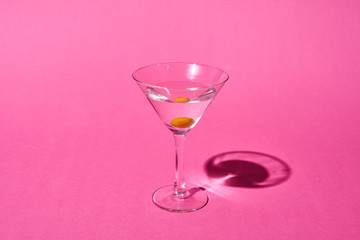 transparent glass with cocktail and olive on pink background