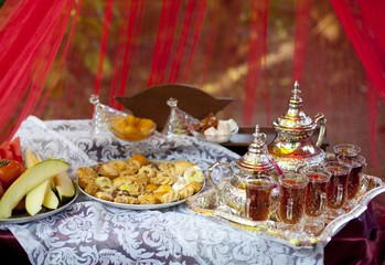 Oriental tea tray and cookies symbolising Moroccan hospitality, Islamic holidays food with decoration. Ramadan kareem. Eid mubarak. Oriental hospitality concept. Tea glasses and pot, traditional delig
