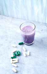 Glass of Protein Shake with milk and blueberries, Beta-alanine and L-Carnitine capsules in background. Sports bodybuilding nutrition. Stone / wooden background.  Copy space.  