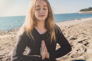 Happy relaxed young woman meditating in a yoga pose at the beach