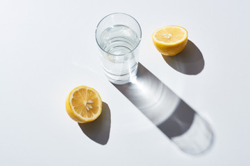transparent glass with water near lemon halves on white background
