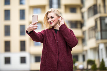 Carefree and happy, sunny spring mood. Charming young lady is making selfie on a camera. She is...