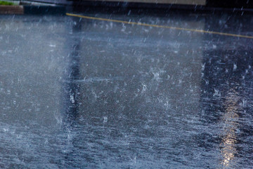 the pouring rain, with a thunderstorm and a thunder, water flows on asphalt forming pools, drops of a rain get to pools and splashes fly rereflecting light from the sun