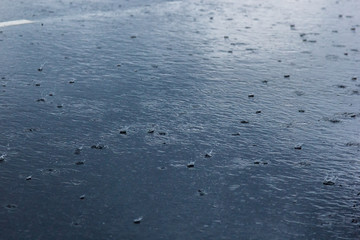 the pouring rain, with a thunderstorm and a thunder, water flows on asphalt forming pools, drops of a rain get to pools and splashes fly rereflecting light from the sun
