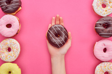partial view of woman holding chocolate doughnut on bright pink background