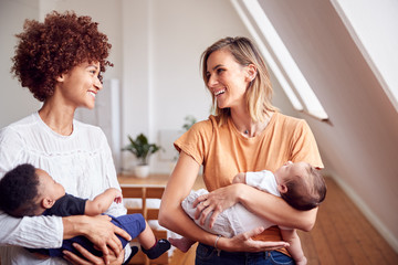 Two Mothers Meeting Holding Newborn Babies At Home In Loft Apartment