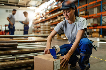 Female worker using tape dispenser gun while packing boxes for the shipment.