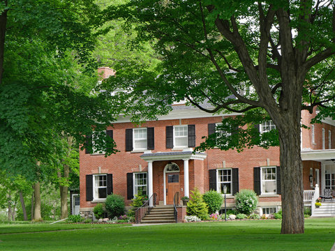 large two story brick suburban house surrounded by trees