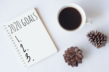 Text 2020 goals on notebook with cup of coffee and pine cone on white background,office desk.