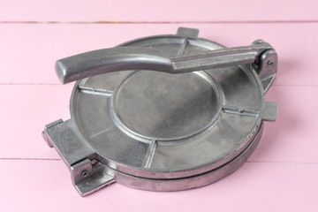 Metallic manual machine tortilla press on pink background