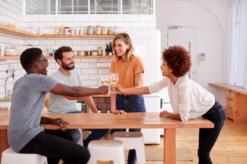 Two Couples Relaxing In Kitchen At Home Making A Toast With Glass Of Wine Together