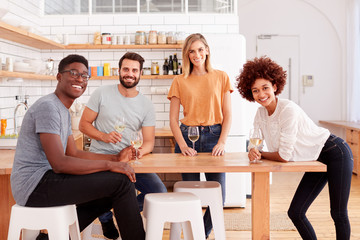 Portrait Of Two Couples Relaxing In Kitchen At Home With Glass Of Wine Together