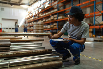 Black female warehouse worker examining steel bars in distribution warehouse.