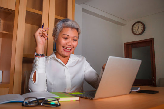 corporate job lifestyle portrait of happy and successful attractive middle aged Asian woman working at office laptop computer desk satisfied and efficient in business success