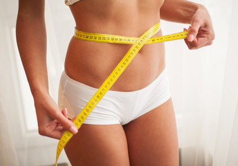 Hands measuring waist with a tape. Slim and healthy woman at her home