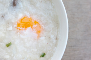 Rice porridge or congee with egg in white bowl on vintage wooden table background.