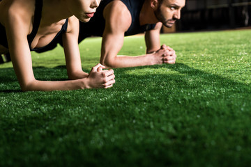 cropped view of woman doing plank exercise with handsome man on grass