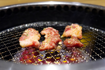 Yakiniku or Japanese grilled barbecue beef. Three pieces of marinated raw beef were put on grill with flame under the grill. Delicious food in Japan,