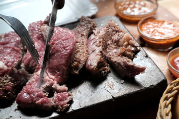 Steak beef on hot lava stone. The raw beef rib eye steak was sliced into pieces by knife cooking on the hot stone with vary dipping sauces in background. Delicious food concept.