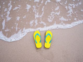 Fototapeta na wymiar yellow sandal on beige sand summer beach background.