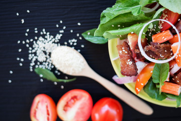 Healthy vegetable salad With fresh tomatoes, onions, lettuce, crab sticks, roasted pork with less fat and sesame on the plate On a black background, food menu, top view - picture