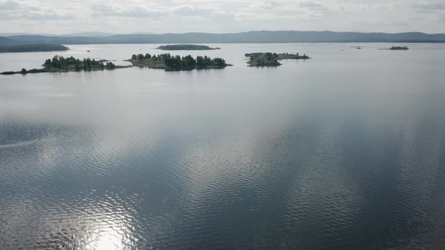 Aerial view; drone flying forward over flooded terrain with uninhabited island and wild flora and founa; untouched nature national in park in Ural; sunset evening time; boat trip between curved coasts