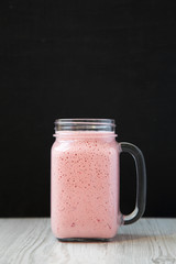 Mason glass jar mug filled with strawberry banana smoothie, side view. Close-up.