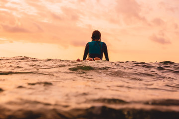 Attractive surf girl with perfect body on surfboard in ocean. Surfing at sunset time