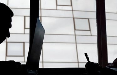 Silhouette of  a man keyboarding on laptop computer, while is sitting in modern office interior.