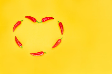 Heart shaped red chili peppers on yellow background with copy space. Passionate love concept.