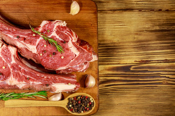 Raw fresh beef rib eye steak on bone with spices, garlic and rosemary on wooden table. Top view